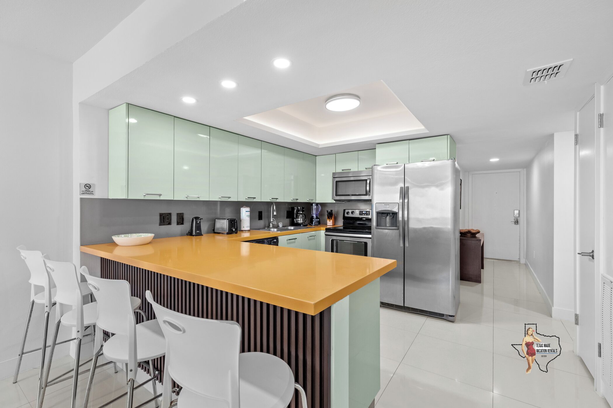 A modern kitchen with a central island, white bar stools, and stainless steel appliances.