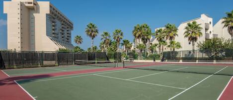 A tennis court with a net, surrounded by palm trees and a building.