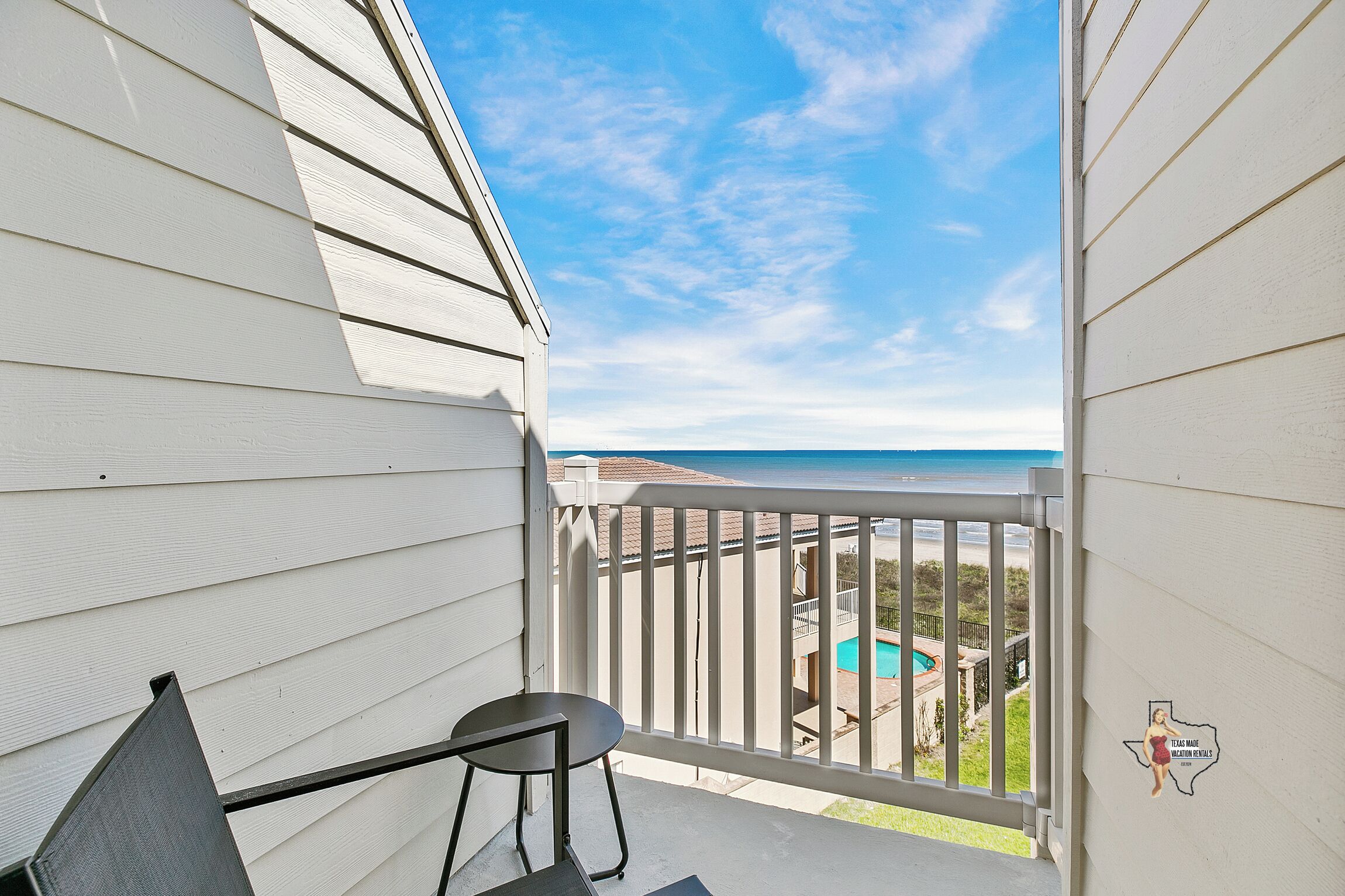 A balcony with a view of a swimming pool and a beach.