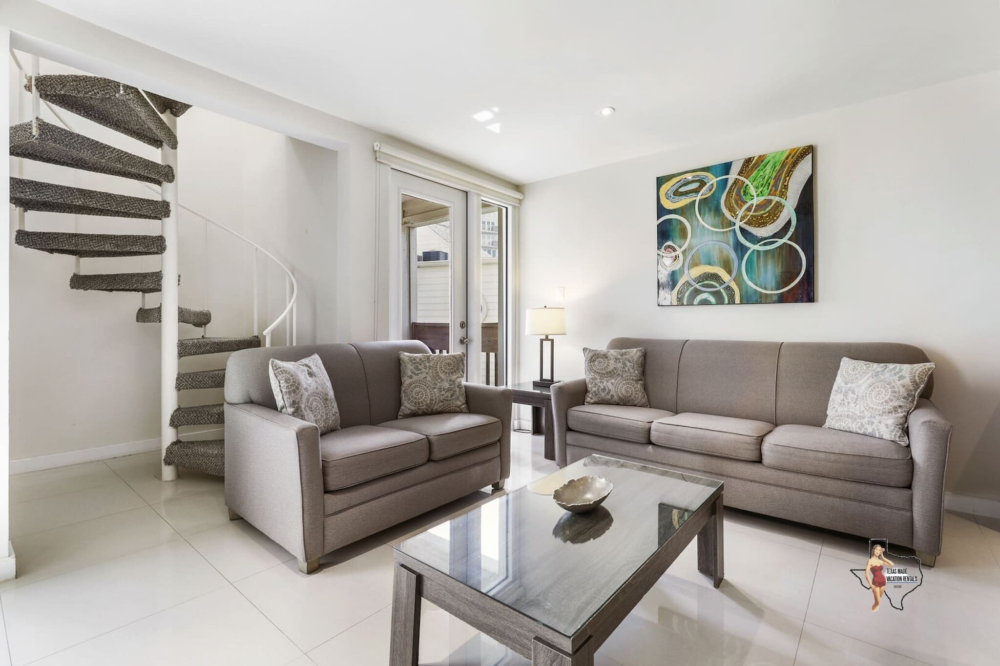 A modern living room with a spiral staircase, two sofas, a coffee table, and a large abstract painting.