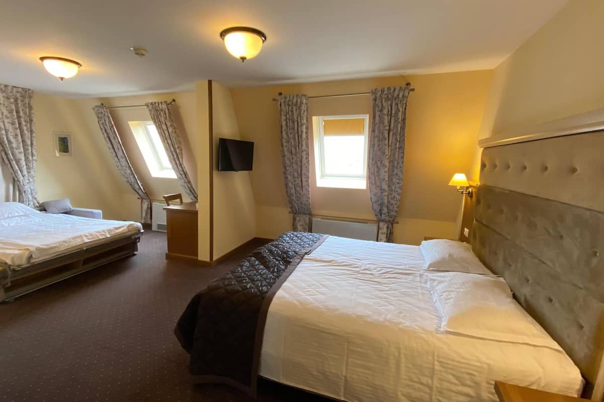 A hotel room with two beds, a flat-screen TV, a window with curtains, and a headboard with a light fixture.
