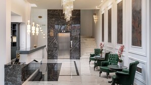A modern lobby with a large chandelier, marble flooring, and green upholstered chairs.