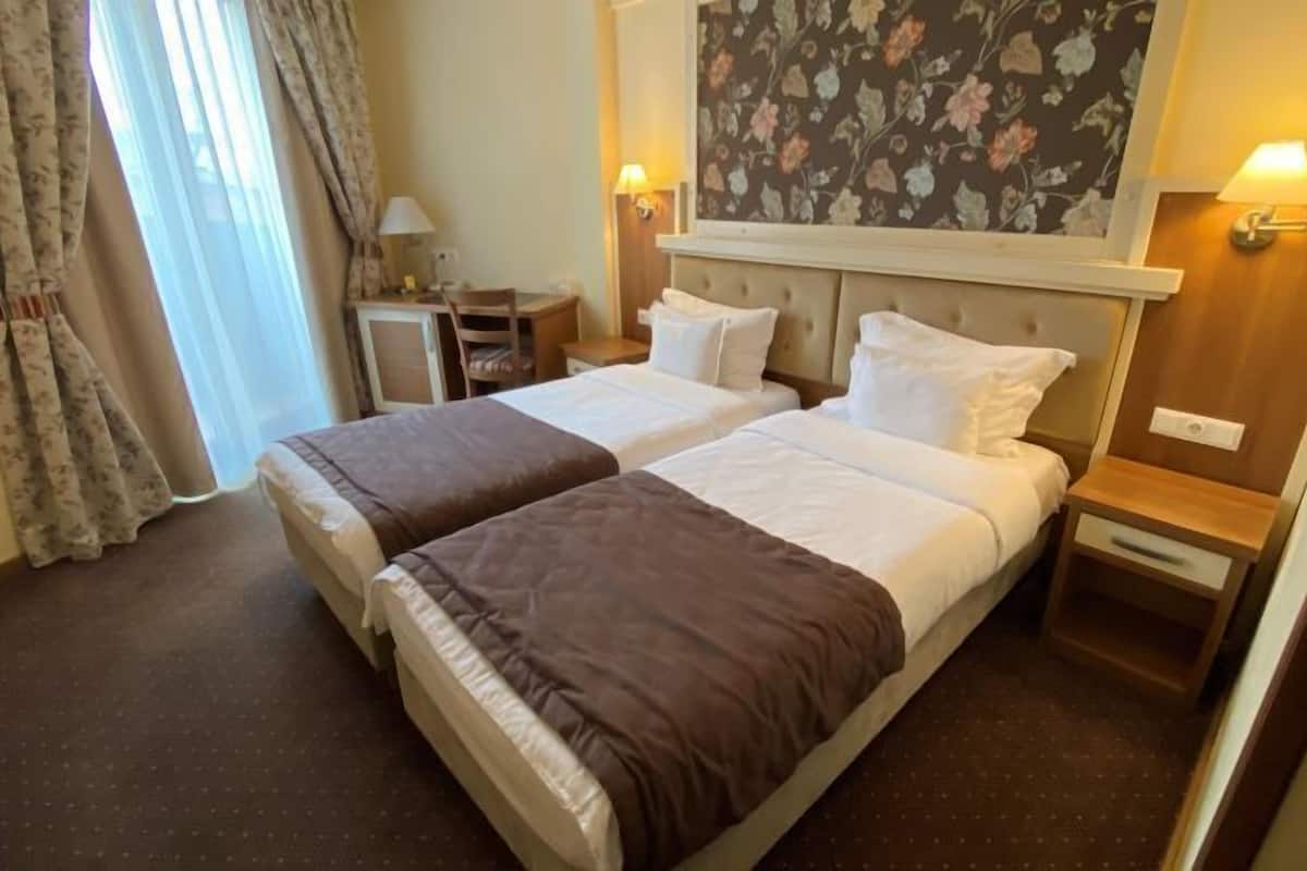 A hotel room with two beds, a desk, a chair, and a nightstand with a lamp.