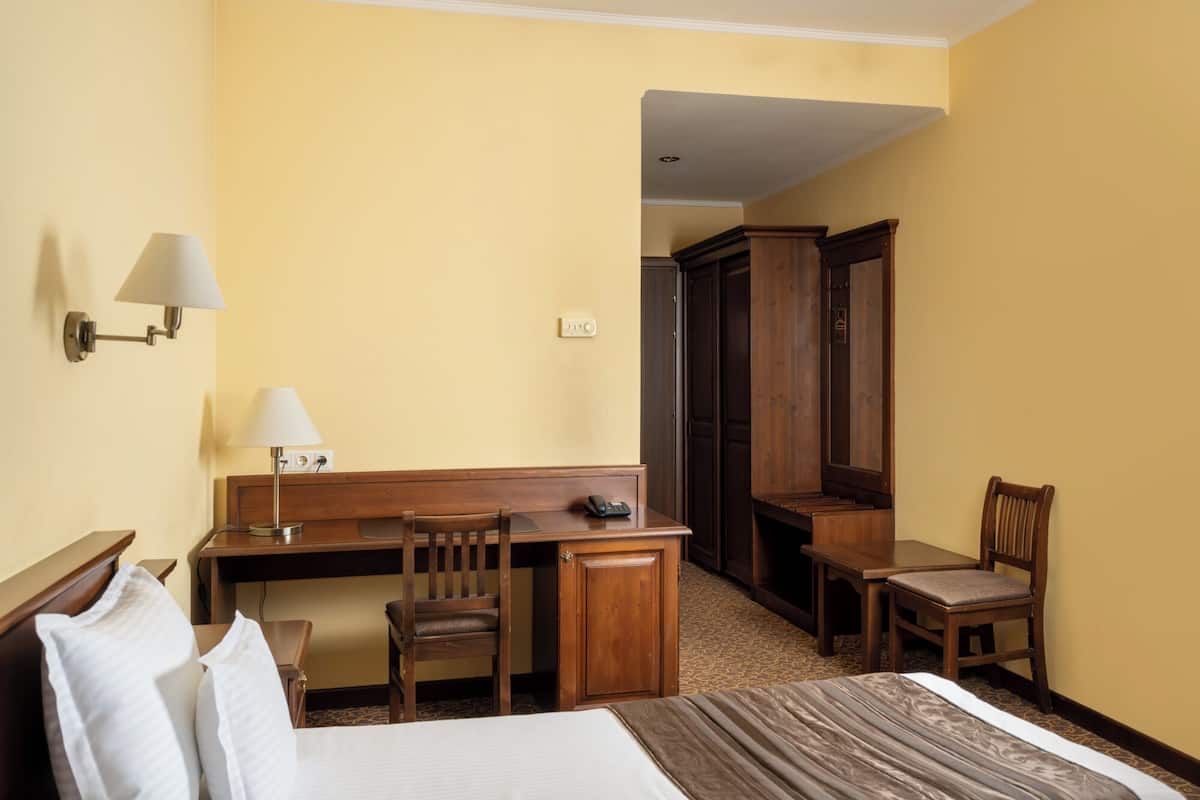 A hotel room with a bed, a desk, two chairs, a telephone, and a lamp.