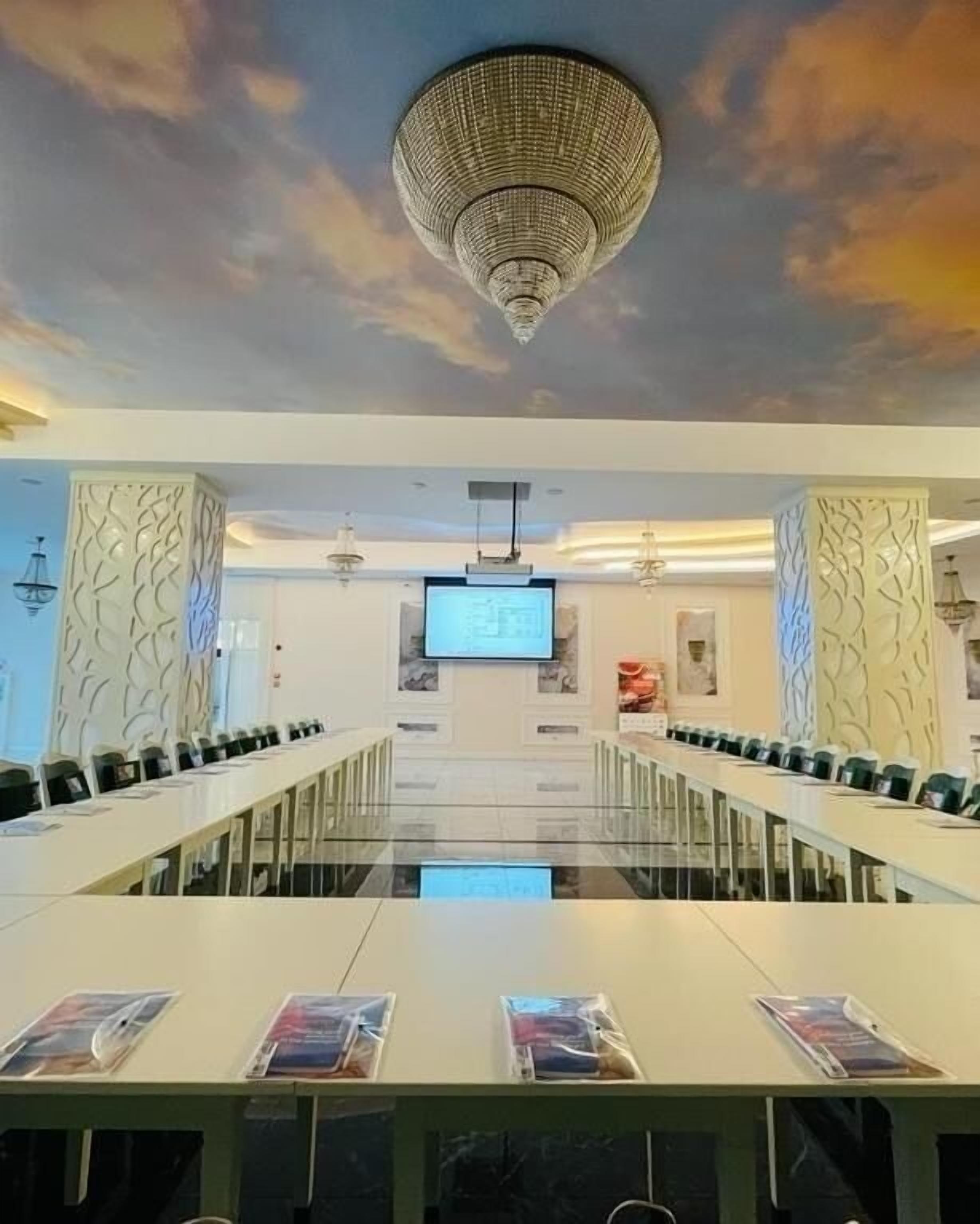 A conference room with a long table, chairs, a screen, and a decorative ceiling.