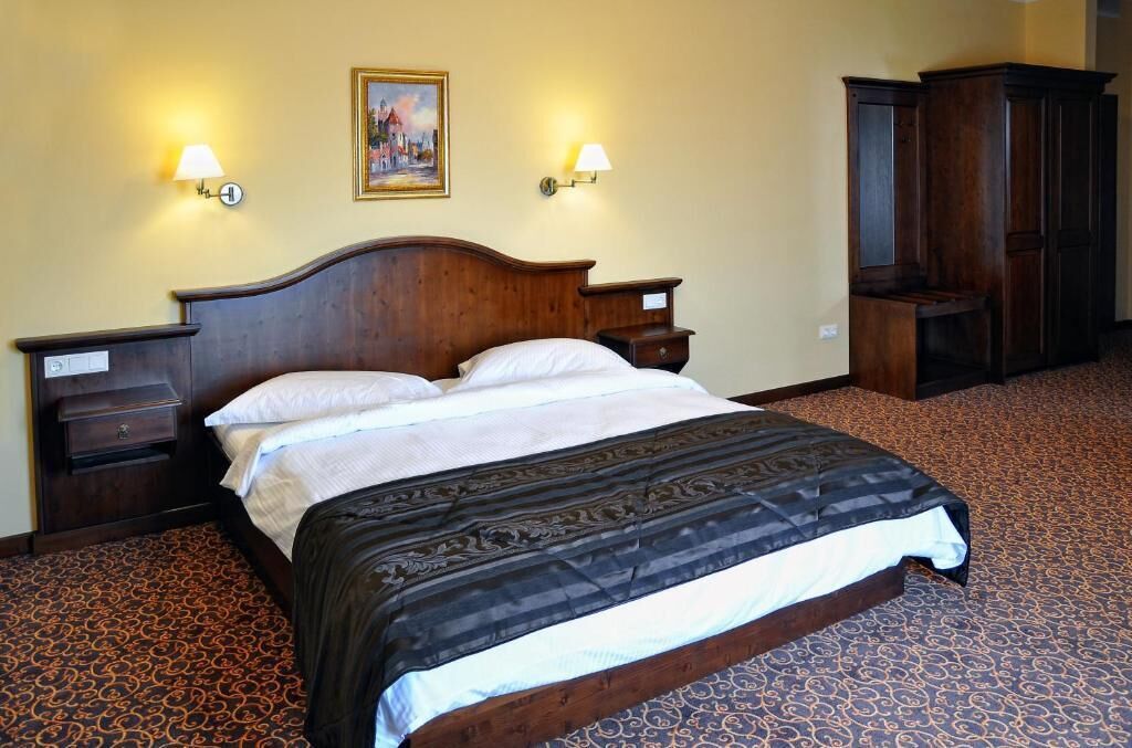 Een hotelkamer met een houten bed, twee nachtkastjes, een kledingkast en twee wandlampen.