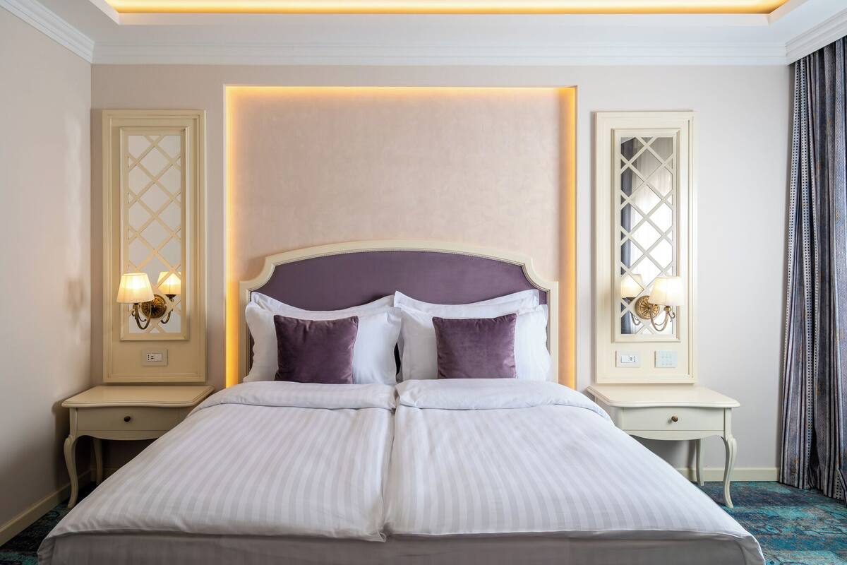 A hotel room with a large bed, two bedside tables, and wall sconces.