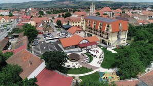 An aerial view of a town with a prominent building featuring multiple floors, a courtyard with outdoor seating, and a parking area.