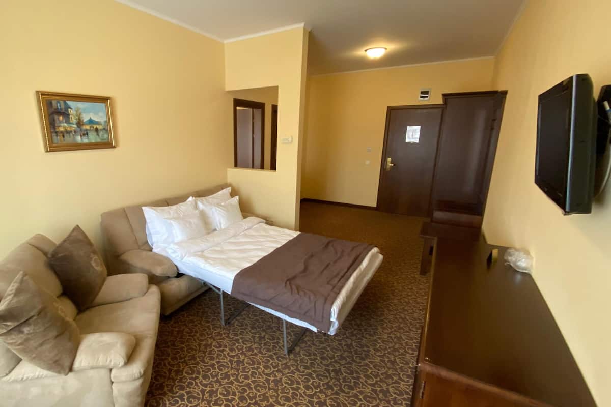 A hotel room with a bed, a sofa, a TV, and a painting on the wall.