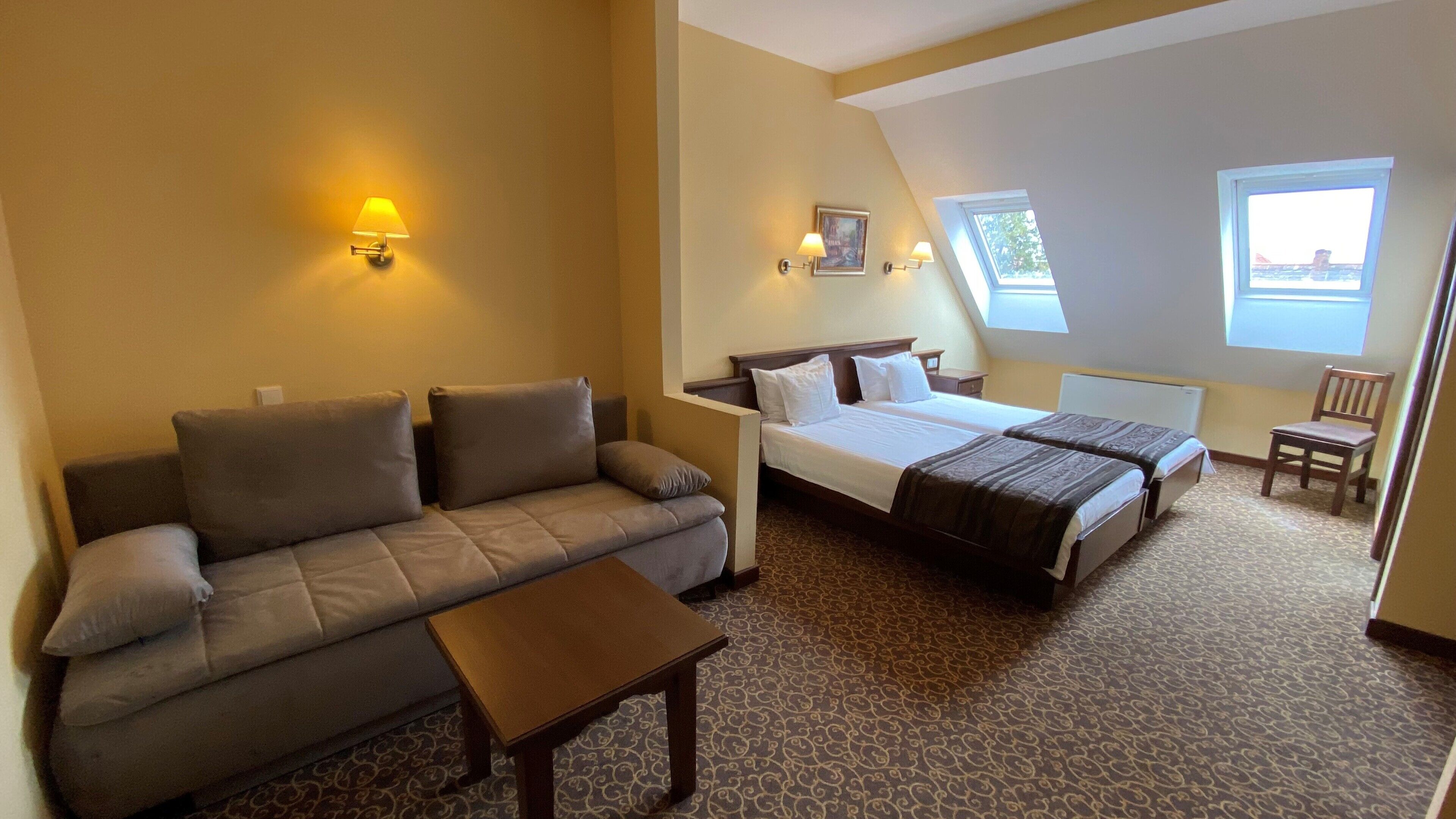 Een hotelkamer met een bank, een bed, een tafeltje en twee ramen.