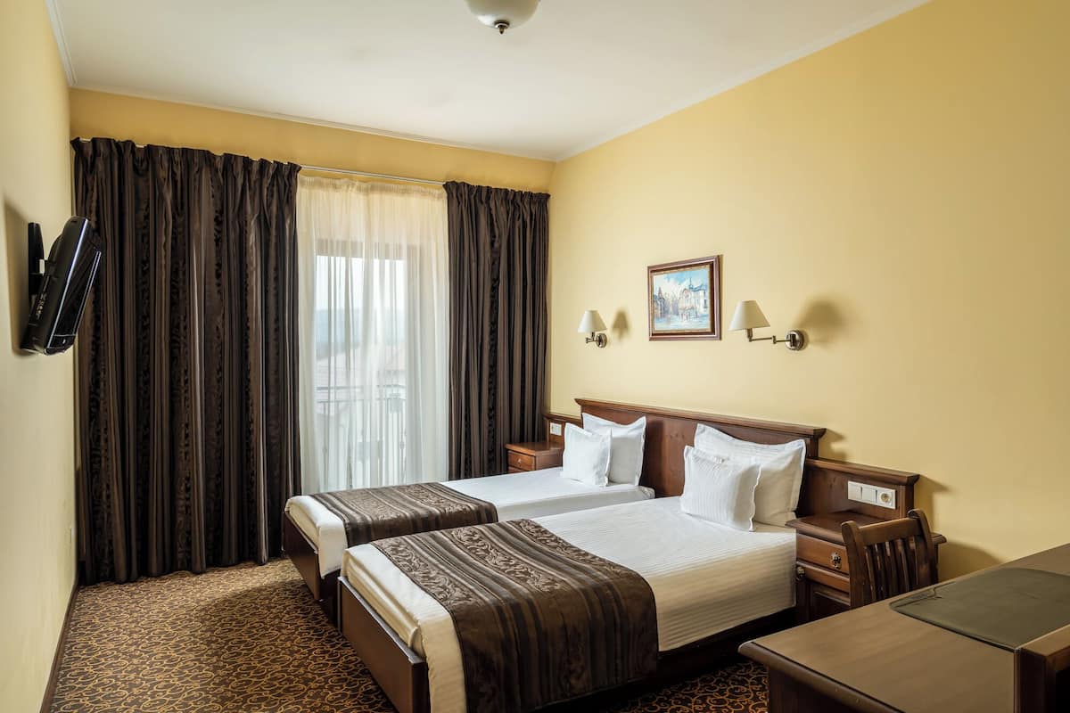 A hotel room with two beds, a desk, a TV, and a painting on the wall.