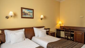 A hotel room with two beds, a desk, a chair, and a painting on the wall.