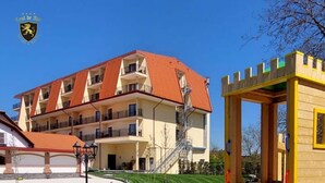 A playground with a climbing wall and a slide, a building with a red roof, and a clear blue sky.