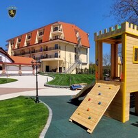 Un parque infantil con pared de escalar y tobogán, un edificio de techo rojo y un cielo azul despejado.