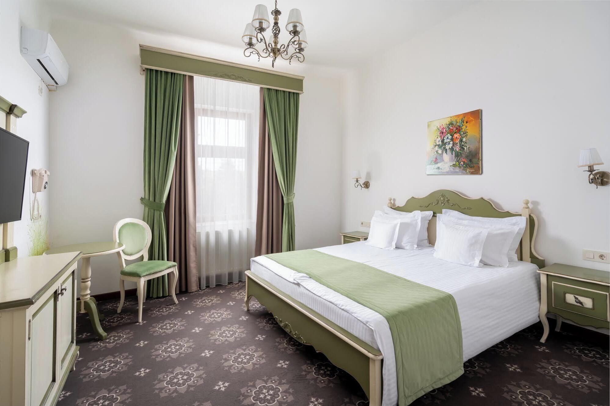 Een hotelkamer met een bed, een stoel, een bureau, een telefoon en een schilderij aan de muur.