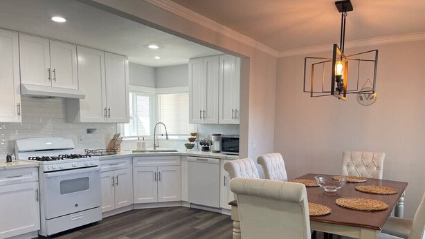 A modern kitchen with white cabinets, a central island, and a dining area with a wooden table and white chairs. - Luxury Stay Near Poppy Fields, Aerospace & Antelope Valley (Lancaster)