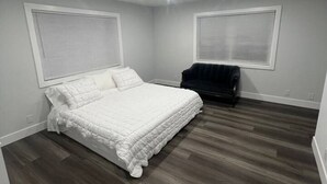 A bedroom with a white bed, dark wood flooring, and two windows with blinds. - Luxury Stay Near Poppy Fields, Aerospace & Antelope Valley (Lancaster)