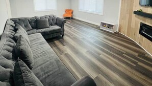 A modern living room with a sectional sofa, a small orange chair, and a TV mounted on a wooden wall. - Luxury Stay Near Poppy Fields, Aerospace & Antelope Valley (Lancaster)