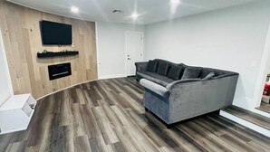 A modern living room with a grey sofa, wooden flooring, and built-in TV. - Luxury Stay Near Poppy Fields, Aerospace & Antelope Valley (Lancaster)