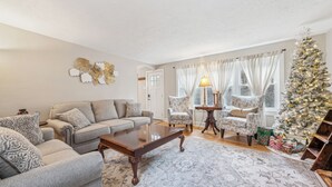 Un salon avec un canapé, des fauteuils, une table basse, un sapin de Noël et une cheminée.