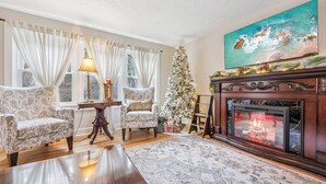 Un salon chaleureux avec des fauteuils à motifs, une cheminée, un sapin de Noël et un tableau accroché au mur.