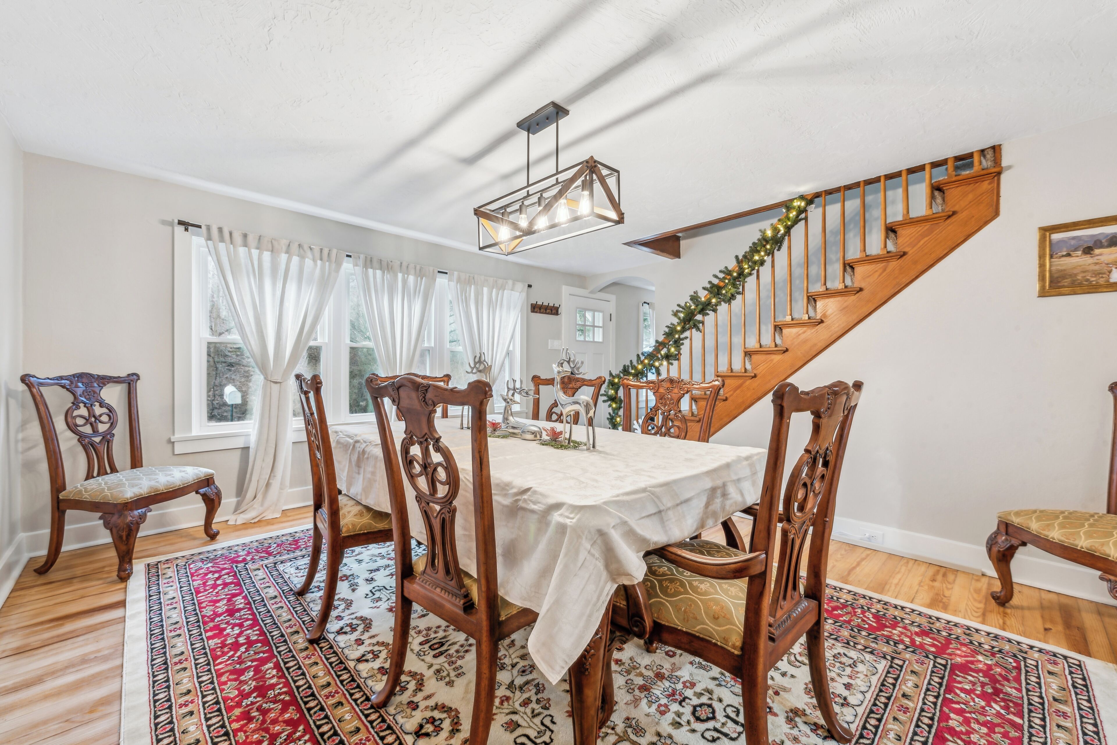 Un espace repas agrémenté d’un escalier en bois, de rideaux blancs et d’un lustre.