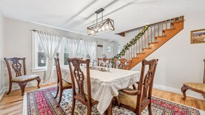 Un espace repas agrémenté d’un escalier en bois, de rideaux blancs et d’un lustre.