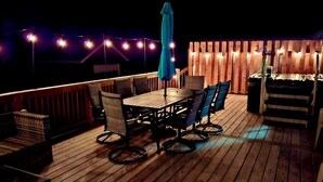 Une terrasse en bois avec une table et des chaises, des guirlandes lumineuses et une clôture en bois.