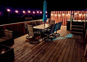 Un terrazzo in legno con tavolo e sedie, luci a stringa e una recinzione in legno.