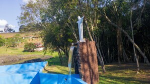 A water feature with a statue, surrounded by trees and a grassy area.