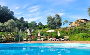 A swimming pool with lounge chairs and umbrellas, surrounded by lush greenery and a stone building. - Agriturismo I Pitti (Serravalle Pistoiese)