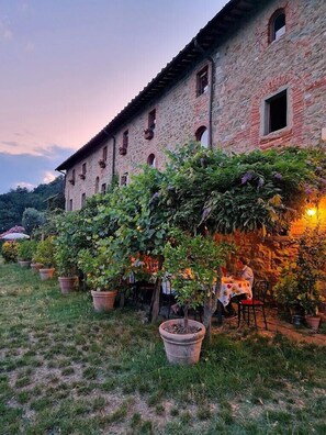 A stone building with a garden area featuring potted plants and a table with chairs. - Agriturismo I Pitti (Serravalle Pistoiese)