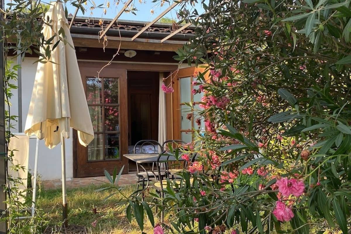 Un jardín con una mesa y sillas, una sombrilla colgante y un edificio con puerta y ventana de madera.
