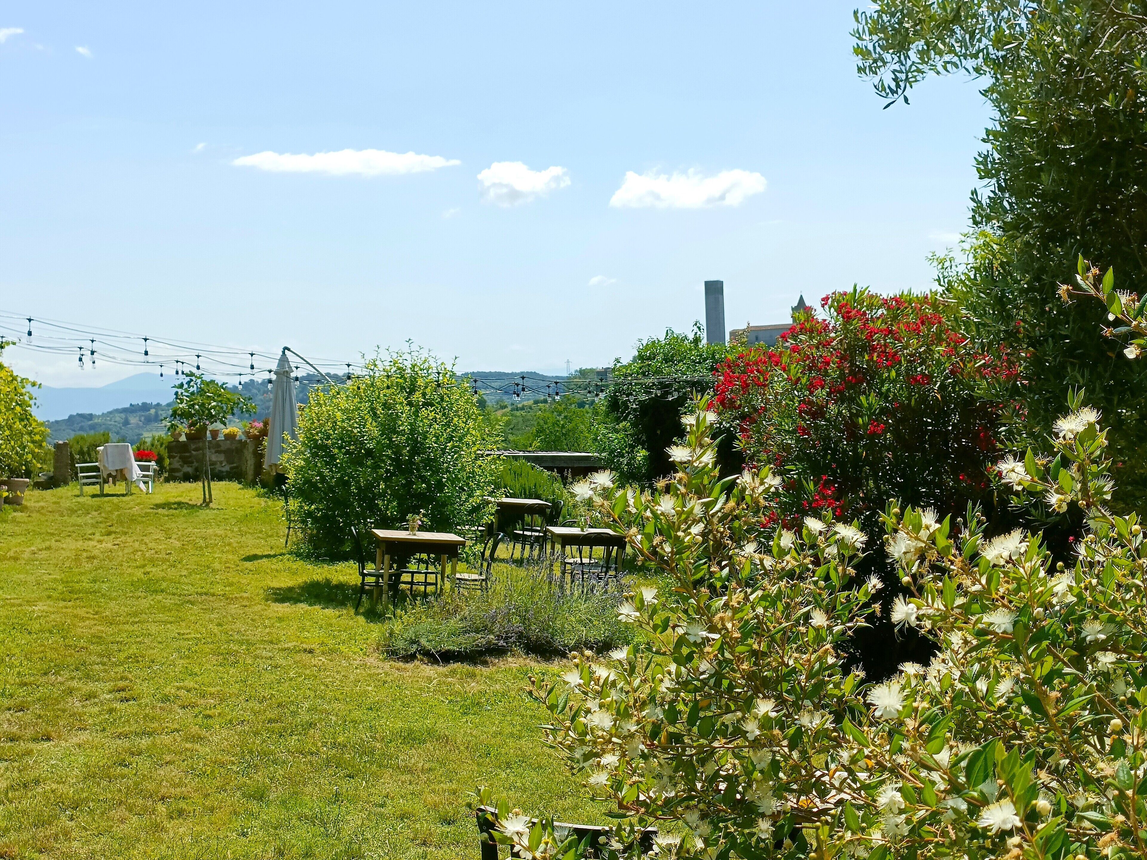 A garden with outdoor seating, a view of the countryside, and a building in the background.