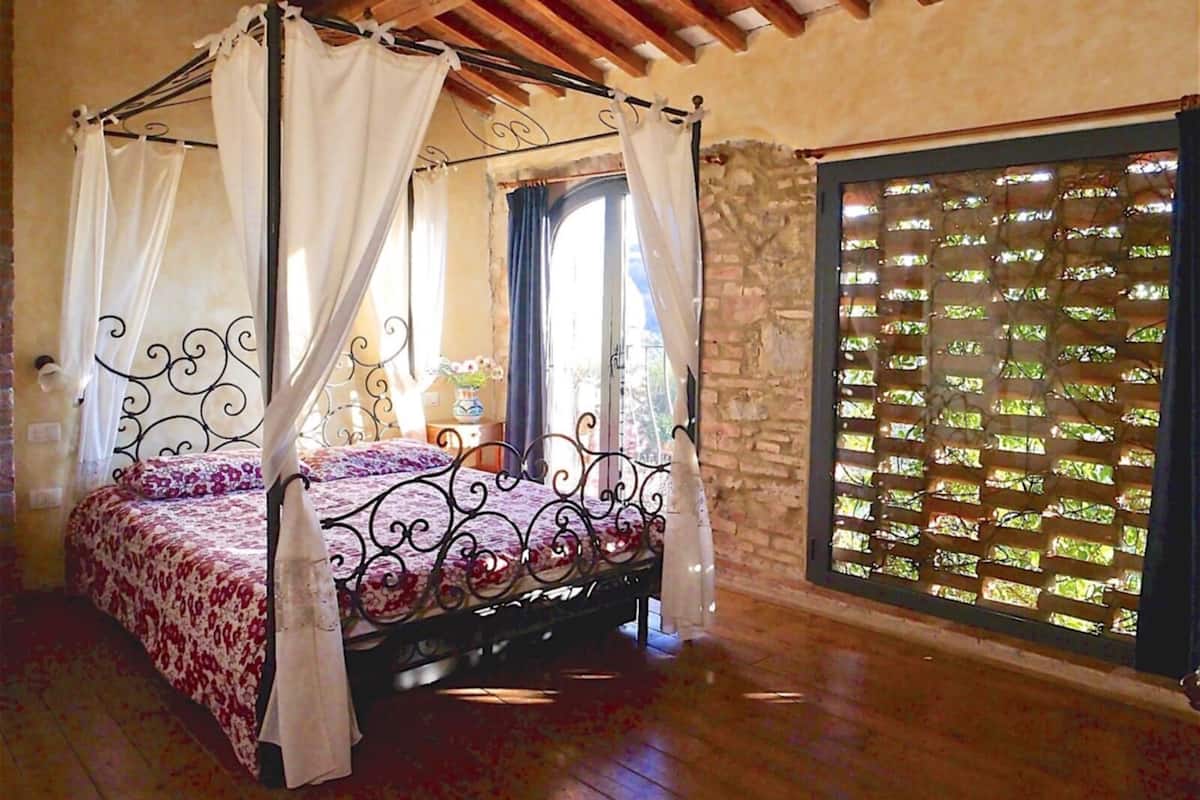 Una cama con dosel adornada con un edredón floral, una pared de piedra y una ventana con celosía.