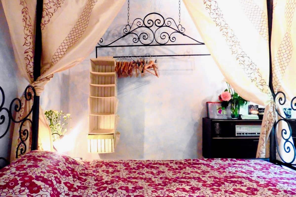 Un dormitorio con cama a dosel, una mesita de noche con radio y un pequeño estante.