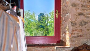 Une vue à travers une fenêtre à cadre rouge, donnant sur un paysage verdoyant et luxuriant, avec des arbres et un ciel bleu clair.