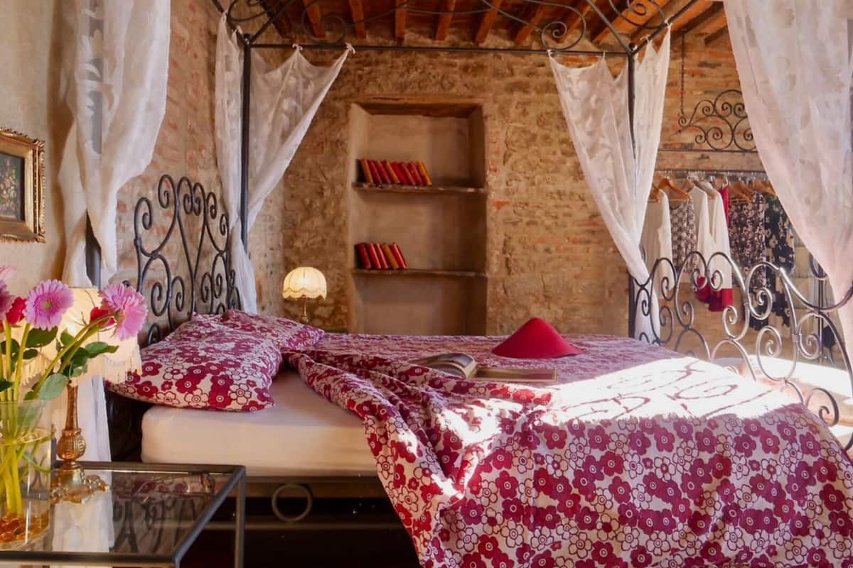 Un dormitorio acogedor con cama con dosel, una mesita de noche con lámpara y una estantería de pared con libros.