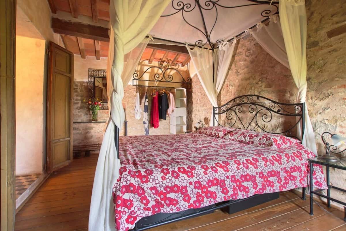 Un dormitorio con cama de dos plazas bajo dosel, piso de madera y pared de piedra.