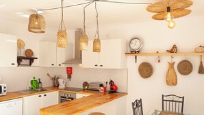 A kitchen with white cabinets, wooden countertops, hanging wicker light fixtures, and a glass dining table with metal chairs. - Candelaria House (Candelária)