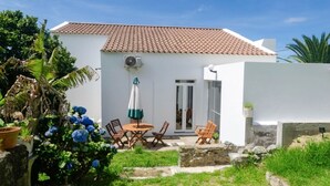 A white building with a tiled roof, a patio with wooden chairs, and a yellow chair in the foreground. - Candelaria House (Candelária)