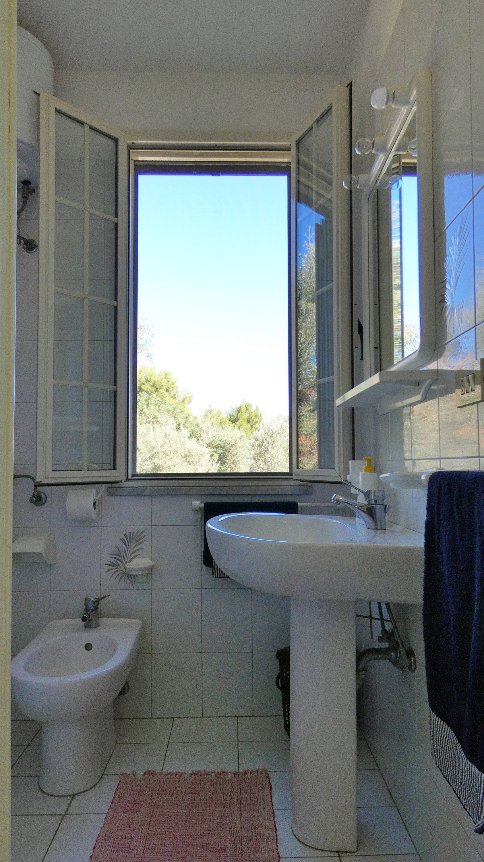 A bathroom with a bidet, a sink, and a window offering a view of trees.