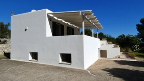 A modern white building with a covered patio area, a stone wall, and a staircase leading to a second level.