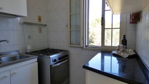 A kitchen with white tiled walls, a gas stove, a sink, and a window with a view of trees.
