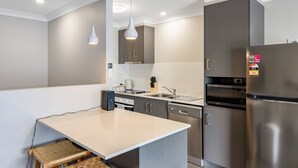 Une cuisine moderne dotée d’un îlot central, d’appareils électroménagers en acier inoxydable et de luminaires suspendus.