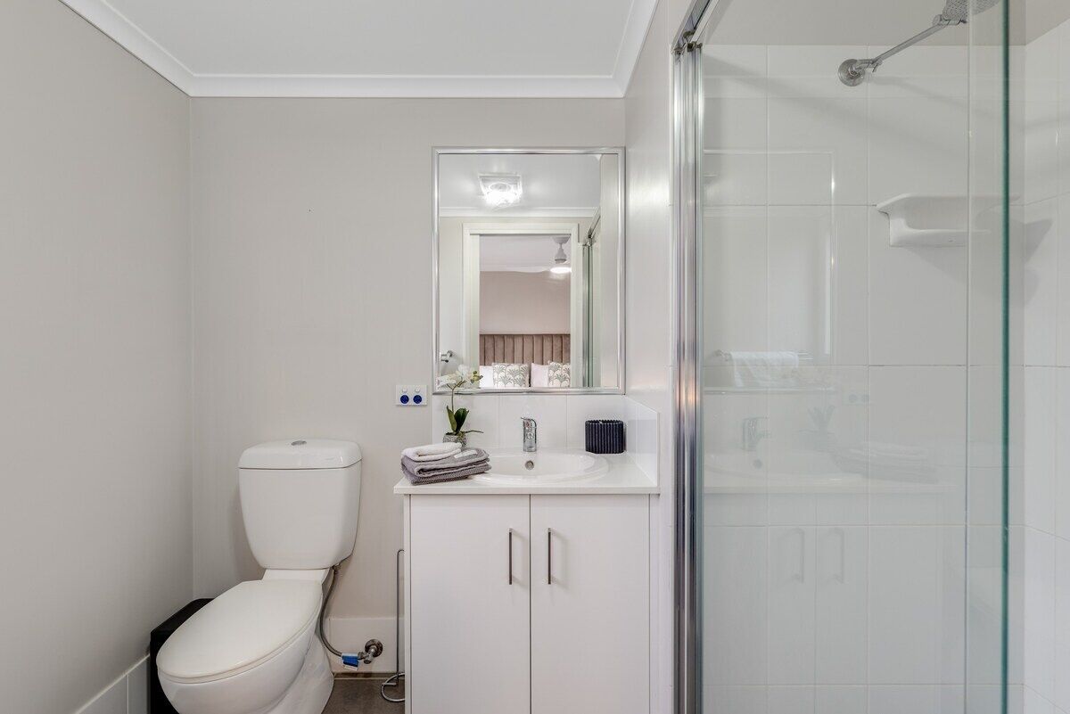 A bathroom with a toilet, a sink, a mirror, and a glass shower enclosure.