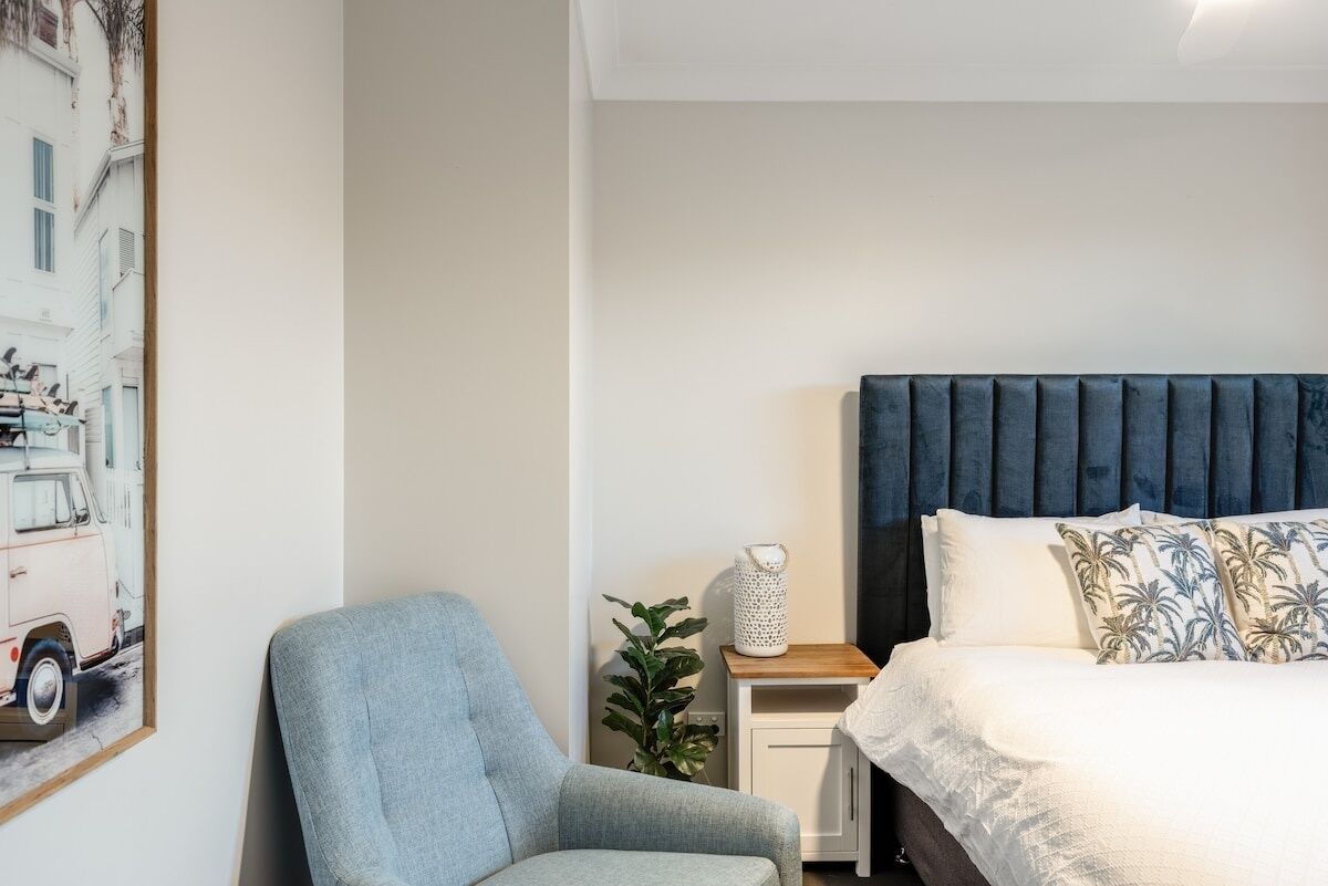 Een slaapkamer met een bed, een stoel, een nachtkastje en een wandlamp.