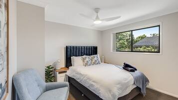 A bedroom with a bed, a chair, a nightstand, a ceiling fan, and a window with a view of trees.