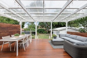 A covered outdoor patio with a wooden deck, a dining table with chairs, and a grey sofa. - Exquisite, Stunning & Central! CDB Fringe Cottage! (Toowoomba City)