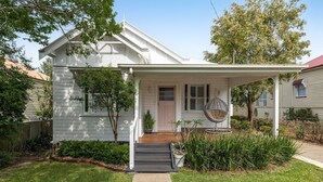 A white single-story house with a covered porch, a front door, and a small front yard with a pathway leading to the door. - Exquisite, Stunning & Central! CDB Fringe Cottage! (Toowoomba City)